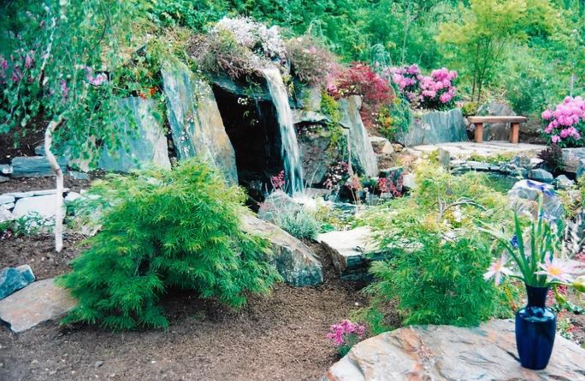 Hidden grotto hot tub with overhead waterfall spilling into natural swimming pool, slate stone boulders. Award winner, Carmel Valley Garden Show.